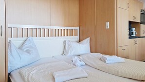 A hotel room with two beds, a wooden headboard, a kitchenette, and a wooden wardrobe.