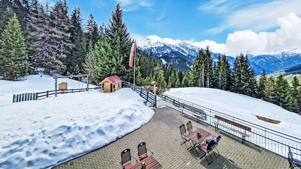 A snow-covered outdoor area with a wooden shelter, a flag, and a paved patio with seating.
