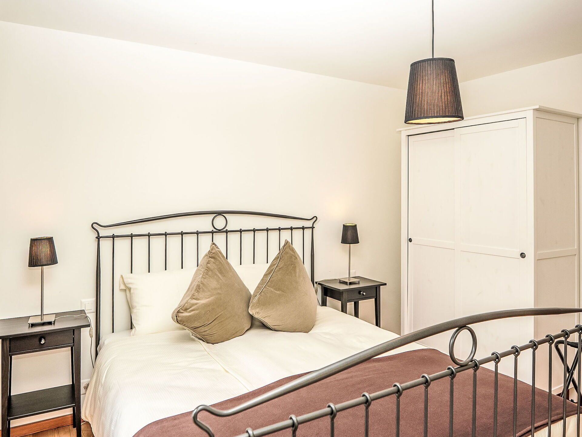 Een slaapkamer met een bed, nachtkastjes, een kledingkast en een hanglamp.