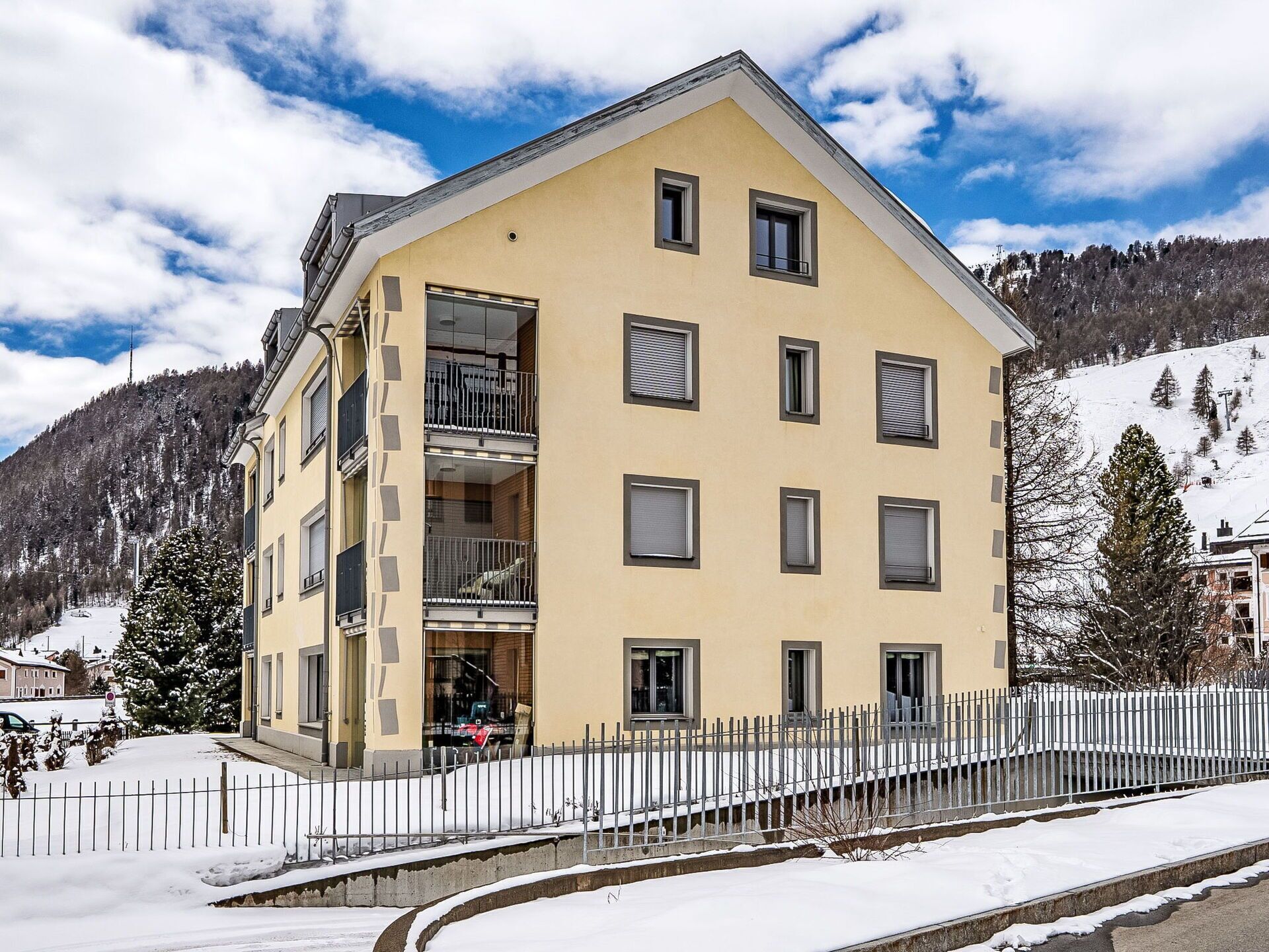 Un immeuble à plusieurs étages doté de balcons, un sol recouvert de neige et un paysage montagneux en arrière-plan.
