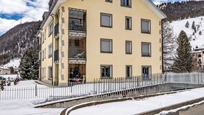 Un immeuble à plusieurs étages doté de balcons, un sol recouvert de neige et un paysage montagneux en arrière-plan.