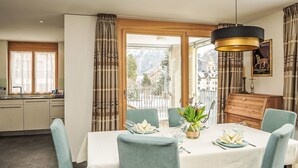 Un coin repas avec une table dressée pour quatre personnes, une vue sur un paysage enneigé par de grandes fenêtres et un meuble en bois doté d’un miroir.