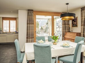 Un coin repas avec une table dressée pour quatre personnes, une vue sur un paysage enneigé par de grandes fenêtres et un meuble en bois doté d’un miroir.