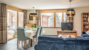 Un salon moderne comprenant un coin repas, de grandes fenêtres, un téléviseur et une bibliothèque.