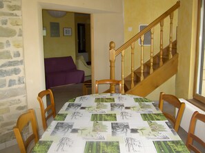 A dining area with a table covered in a botanical print tablecloth, wooden chairs, a wooden staircase, and a purple sofa in the background.