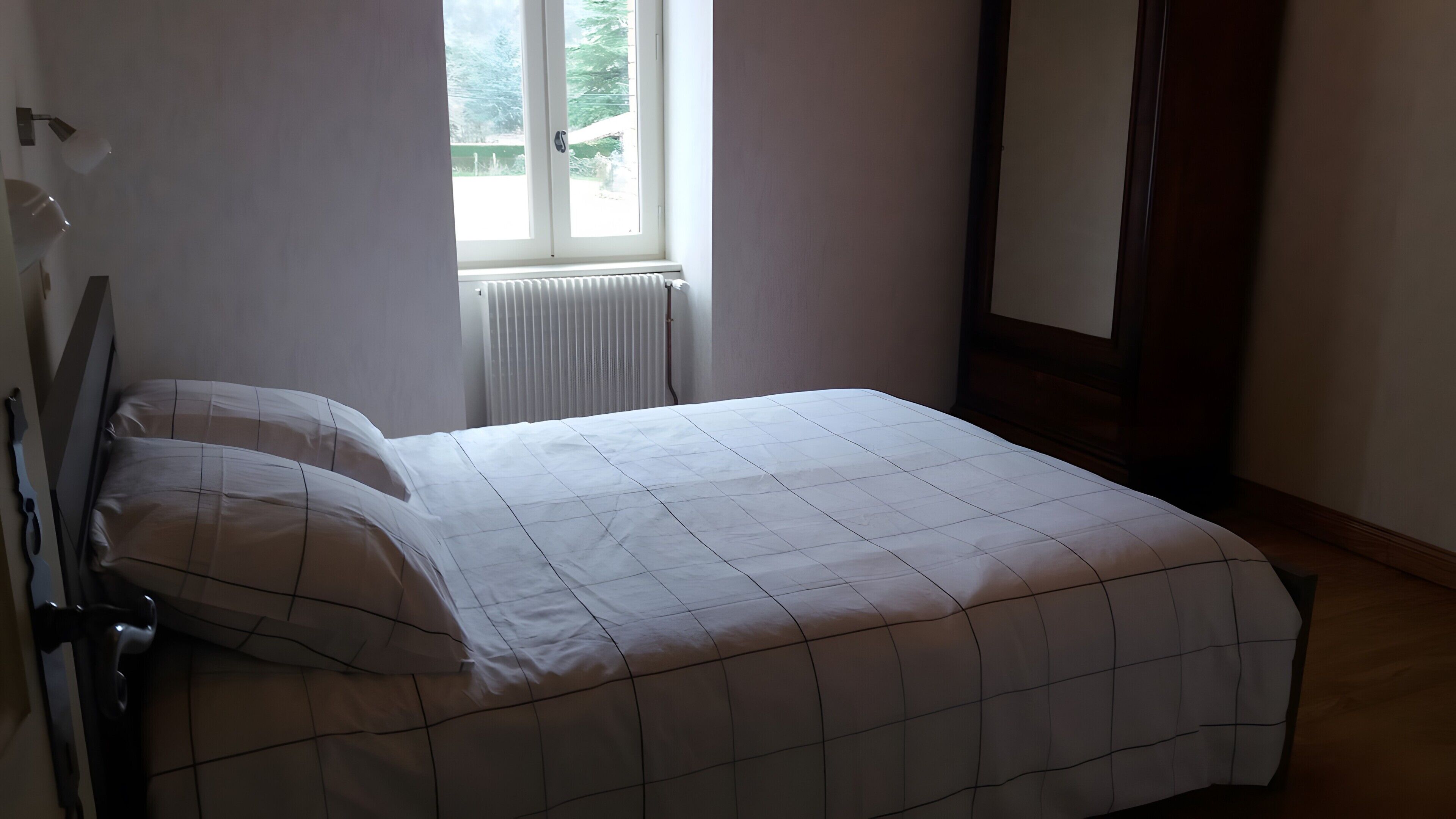 A bedroom with a bed, a radiator, a window, and a door.