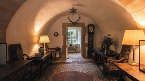Una habitación abovedada con alfombra estampada, muebles de madera, una araña y un reloj de pie.