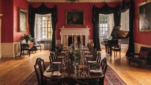 Un comedor formal con una larga mesa dispuesta para una comida, una chimenea y un piano de cola.