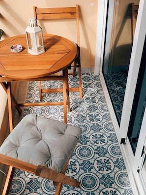 A small wooden table with a white lantern and a decorative item, a cushioned bench, and a patterned floor. - Sunny Studio, Balcony & Fast WiFi · 2 min to Beach (Los Cristianos)