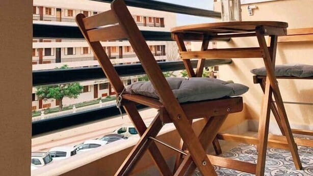 Un balcón con una silla de madera, una mesita y un ventilador de techo.