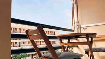 En balkon med en træstol, et lille bord og en ventilator.