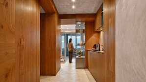Un pasillo interior de madera que conduce a una zona de cocina, donde se ve a una persona a lo lejos.