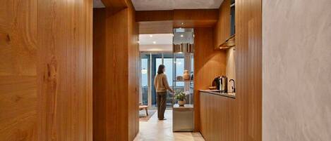 A wooden interior hallway leading to a kitchen area with a person standing in the distance.