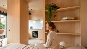 Un interior moderno con una cama, horno empotrado, estanterías de madera y una planta colgante.