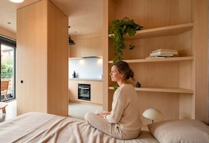 A modern interior with a bed, a built-in oven, wooden shelving, and a hanging plant. - Sunny Studio, Balcony & Fast WiFi · 2 min to Beach (Los Cristianos)