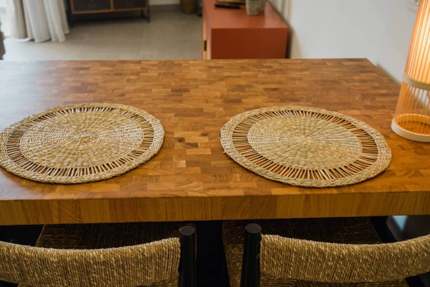 Een houten eettafel met twee gevlochten placemats en rieten stoelen.
