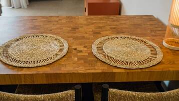Een houten eettafel met twee gevlochten placemats en rieten stoelen.