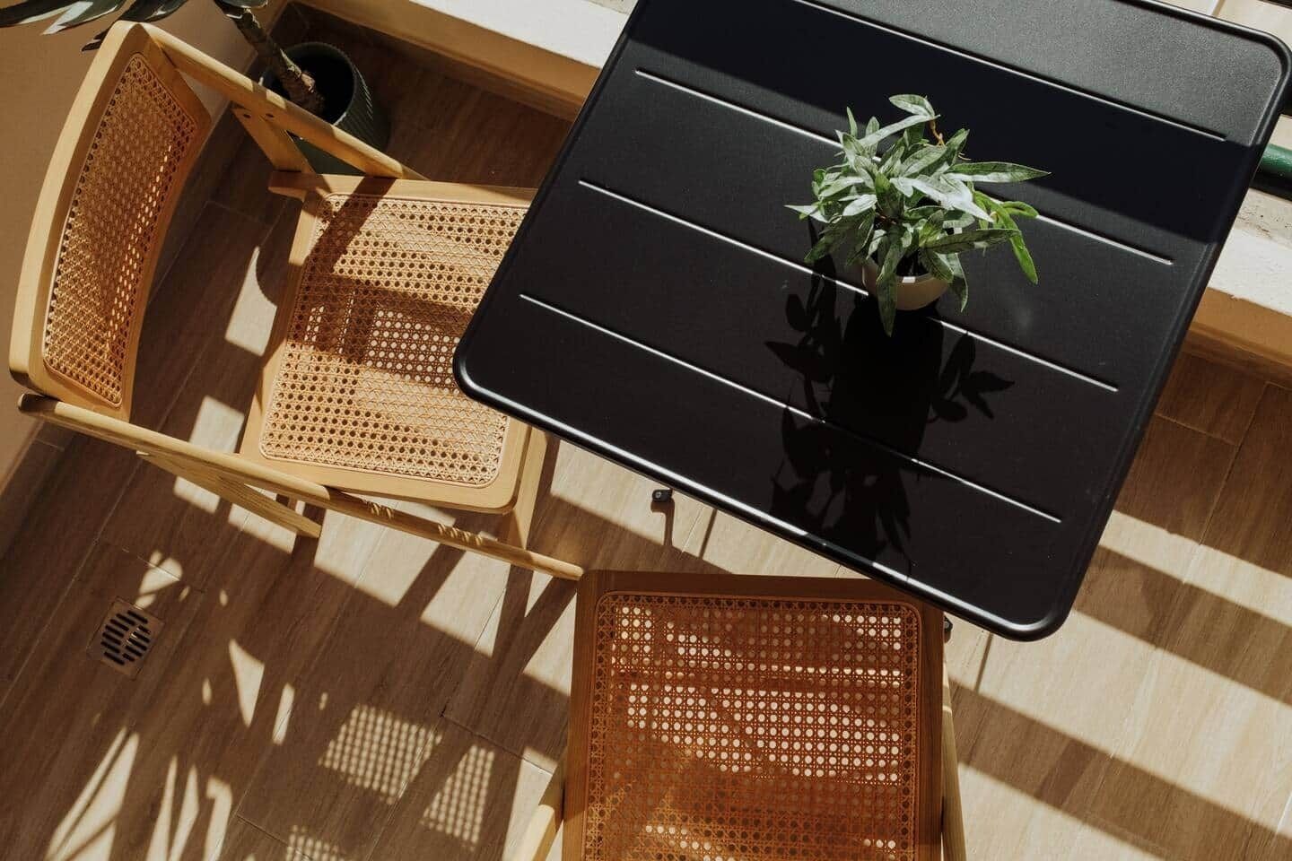 Une table avec une plante en pot, des chaises en osier et un sol parsemé d’ombres.