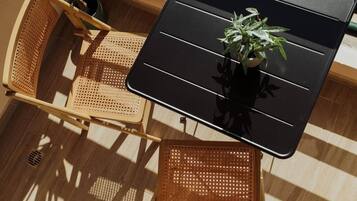 Une table avec une plante en pot, des chaises en osier et un sol parsemé d’ombres.