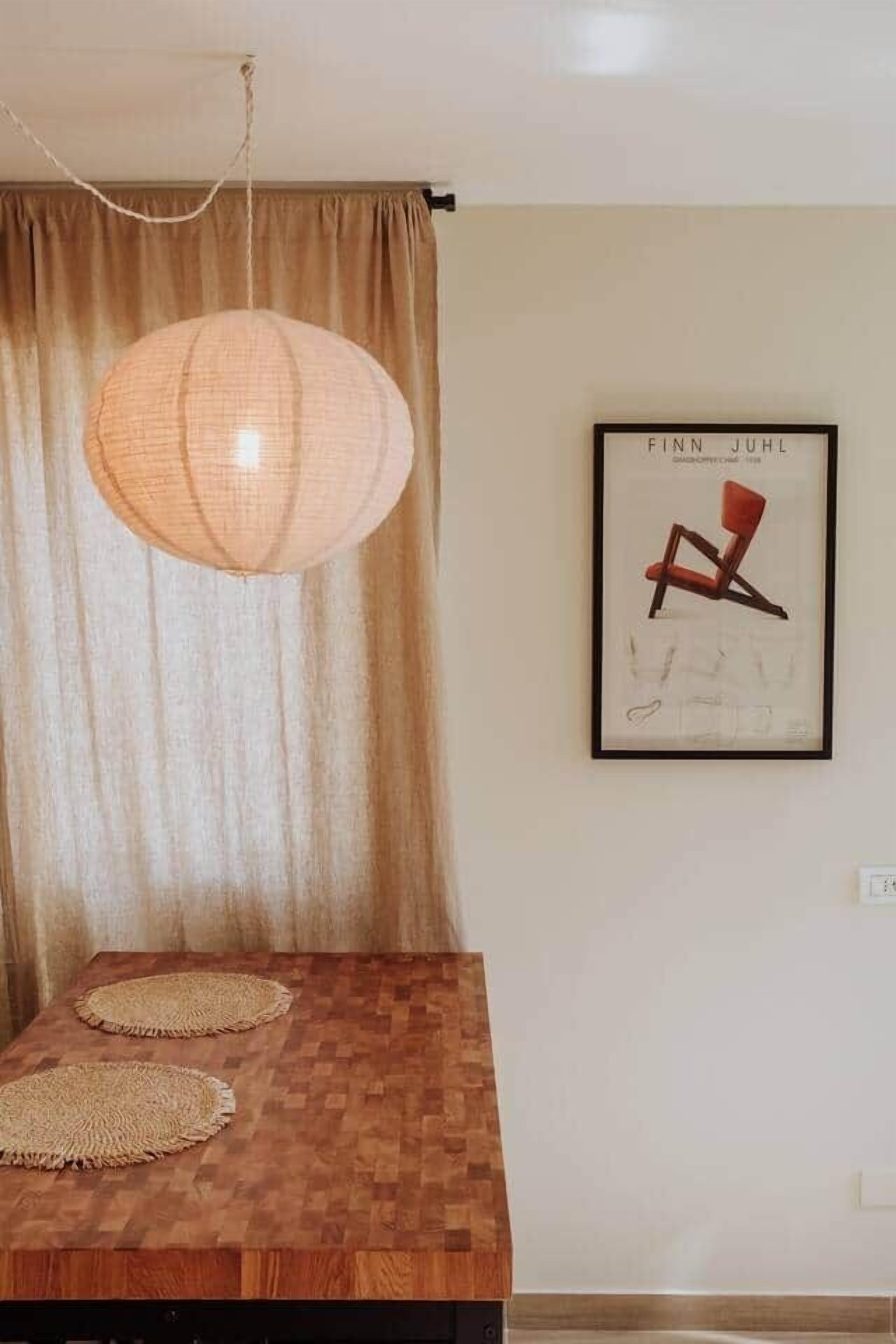 A dining area with a wooden table, woven placemats, a hanging light fixture, and a framed picture on the wall.