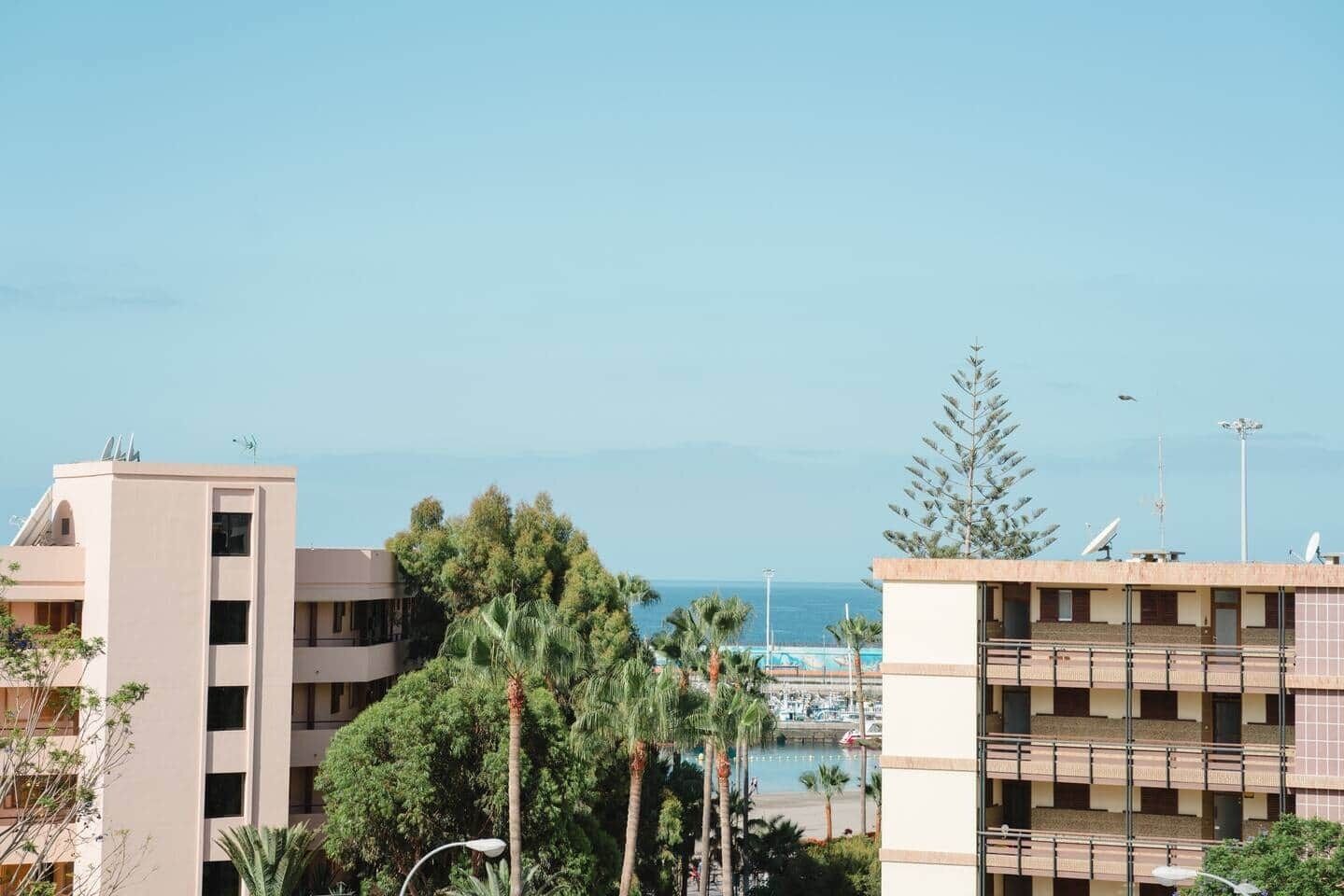 A coastal hotel with multiple floors, a marina in the background, and a clear sky.