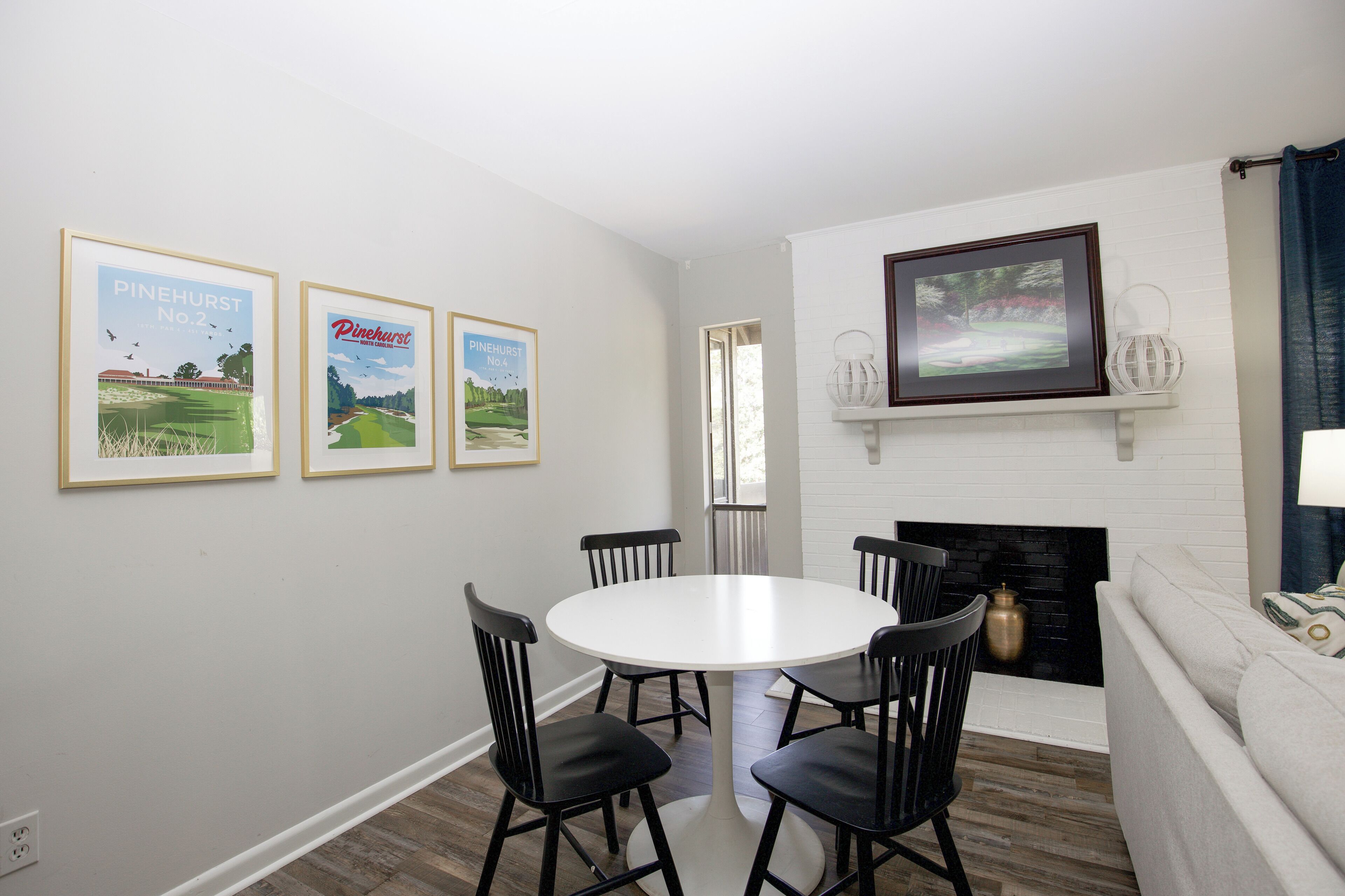 A dining area with a round table and four chairs, a fireplace, and framed pictures on the wall.