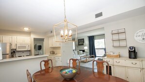 A modern kitchen with white cabinets, a dining table with chairs, a hanging light fixture, and a living area with a sofa and coffee table. - 3-Bedroom Pinehurst Condo at Lakeview with Pool (Pinehurst)