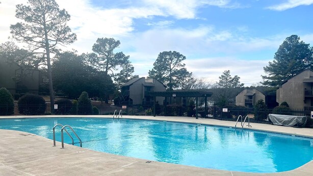 A swimming pool with clear blue water, surrounded by a concrete deck. There are trees and buildings in the background. - 3-Bedroom Pinehurst Condo at Lakeview with Pool (Pinehurst)