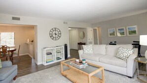 A living room with a white sofa, a coffee table, a bookshelf, and a dining area with chairs and a table. - 3-Bedroom Pinehurst Condo at Lakeview with Pool (Pinehurst)
