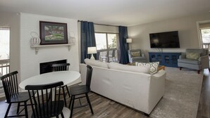 A living room with a white sofa, a dining table with chairs, a TV, and a fireplace. - 3-Bedroom Pinehurst Condo at Lakeview with Pool (Pinehurst)