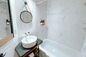 Ein Badezimmer mit weißem Waschbecken, einem Spiegel, einem Handtuchhalter und einer Badewanne.