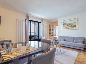 Ein modernes Wohnzimmer mit Essbereich, einer Couch, einem Bücherregal und einem großen Fenster mit Vorhängen.