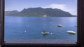 Blick durch ein Fenster auf einen stillen See mit Booten, einen Berg und einen klaren Himmel.