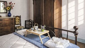 Une chambre à coucher avec un lit, une armoire en bois, une table de chevet avec un plateau, un miroir et un vase avec des fleurs.