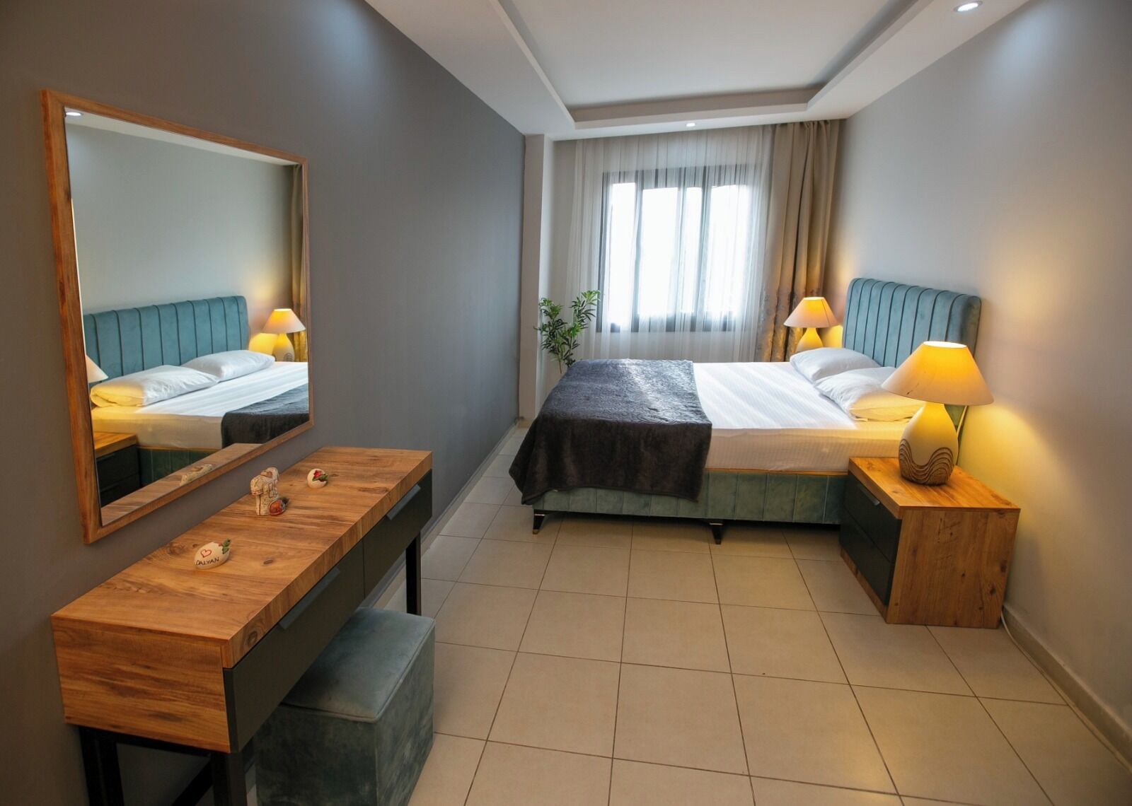 Une chambre d’hôtel avec un lit, une table de chevet, une lampe, un miroir et un petit banc.
