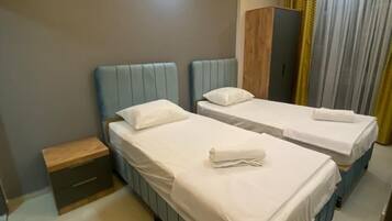 A hotel room with two beds, a nightstand, a wardrobe, and a window with curtains.