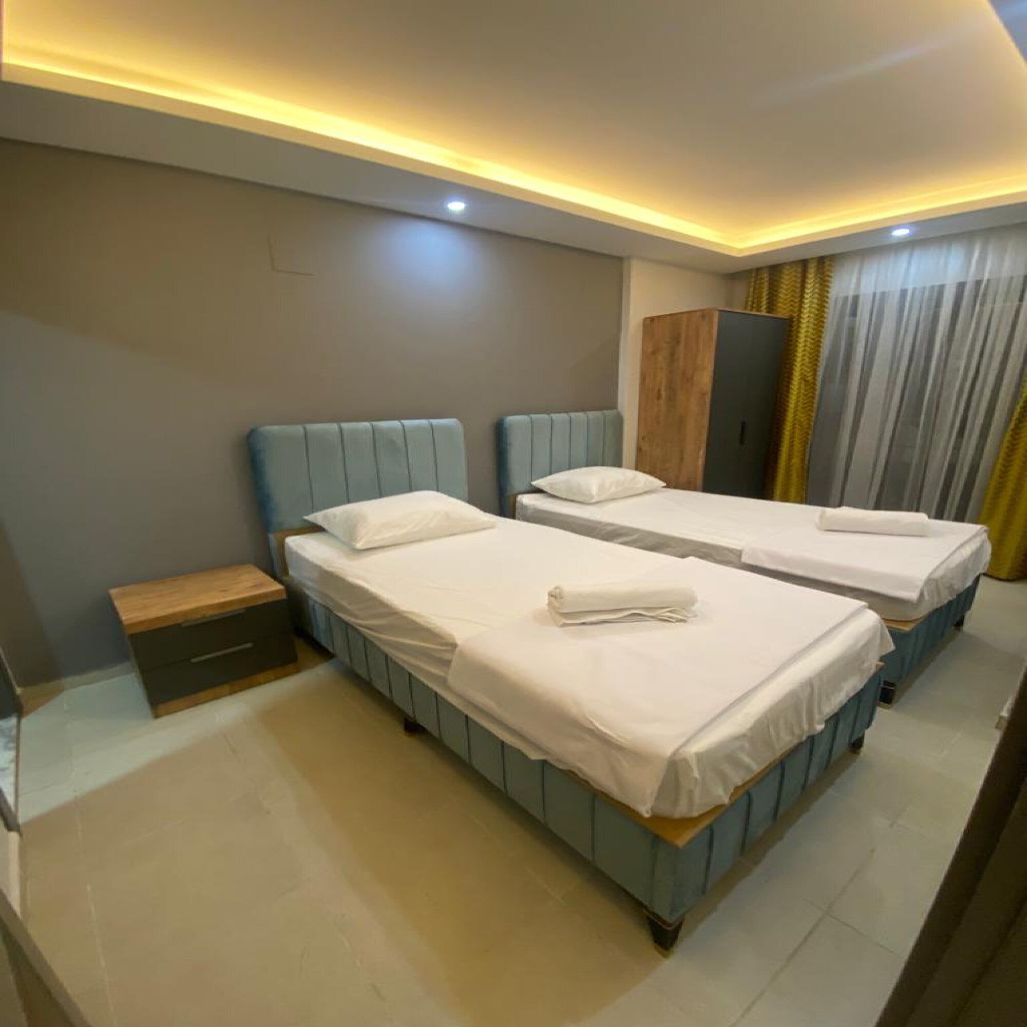 A hotel room with two beds, a wooden nightstand, a wardrobe, and a curtain.