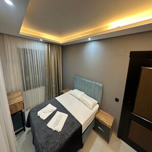 A modern hotel room with a bed, bedside tables, a wooden nightstand, a window with curtains, and a door. - LOCA MARİN OTEL (Kocasinan)