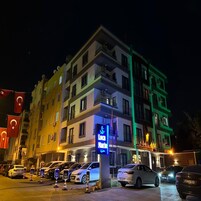 Un hotel de varios pisos con balcones, un letrero visible que dice 'Loca Marina Hotel' y varios coches estacionados en la parte delantera.