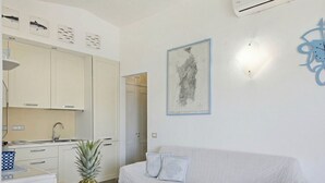 Eine moderne Küche mit weißen Schränken, einem Esstisch mit Obstschale und einem weißen Sofa im Wohnbereich.