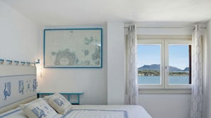 Ein Schlafzimmer mit einem Bett, einer Karte an der Wand, einem Fenster mit Meerblick und einem kleinen Tisch.