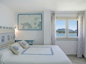 Ein Schlafzimmer mit einem Bett, einer Karte an der Wand, einem Fenster mit Meerblick und einem kleinen Tisch.