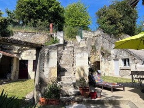Ein Innenhof mit Steintreppen, einer roten Tür, einem Liegestuhl und einem gelben Sonnenschirm.
