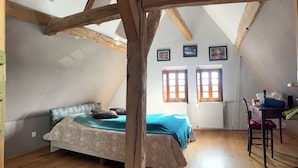 A room with a sloped ceiling, wooden beams, a bed with floral bedding, two windows with shutters, and a radiator. - 16th-century Tourangelle between Beauval and Chenonceaux (Montrichard Val de Cher)