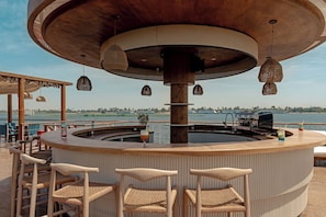 A bar area with wicker chairs, a round bar, and a view of the water.