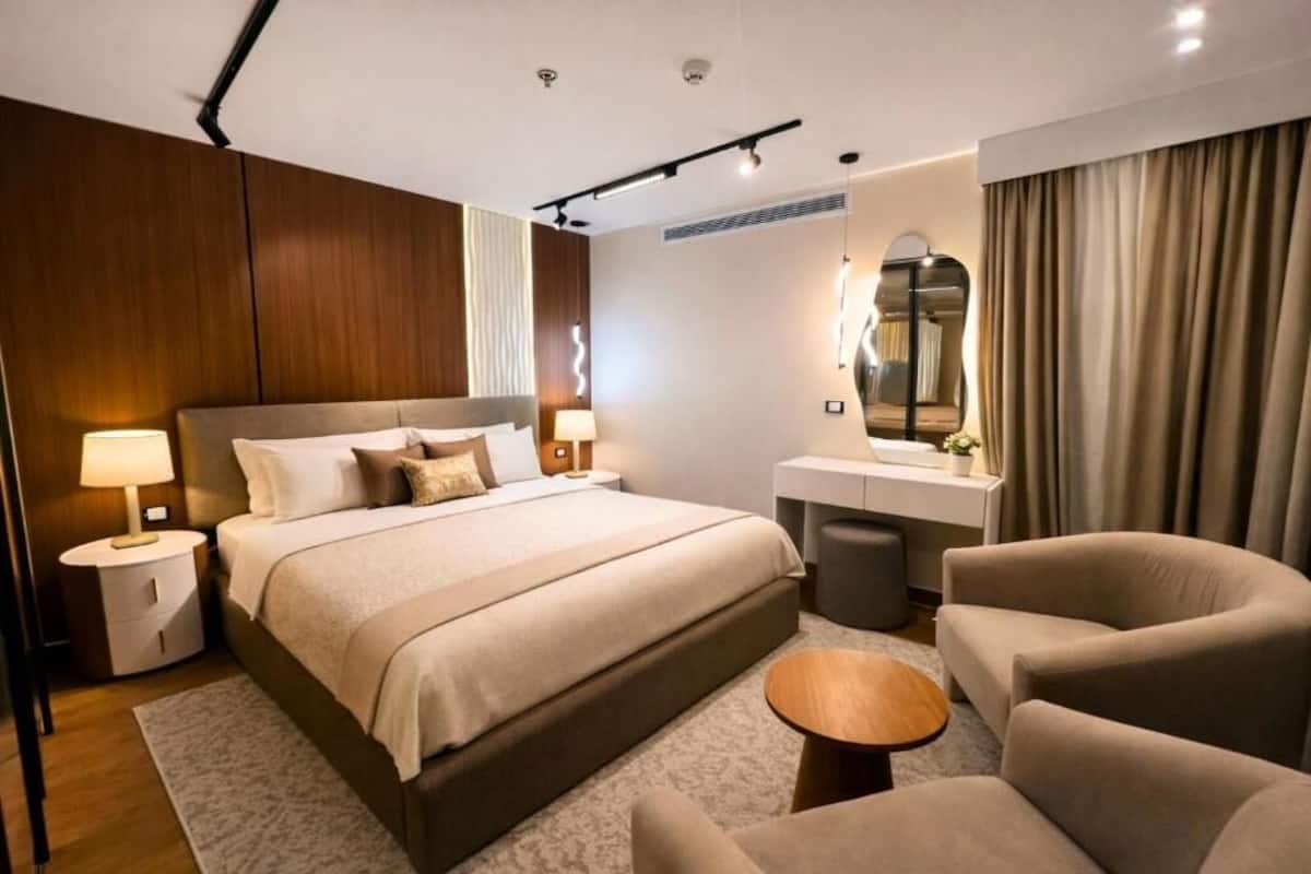 A modern hotel room with a large bed, bedside tables, a vanity, and a seating area.