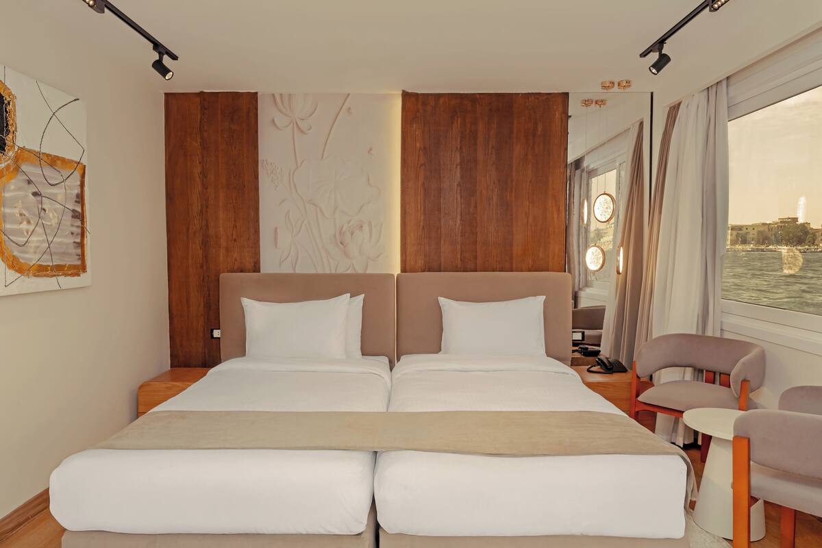 A double bed with a wooden headboard, a bedside table, a chair, and a view of the water.
