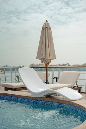 Zona junto a la piscina con sillones de descanso y una sombrilla, con vista a un cuerpo de agua.