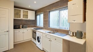 Cocina compacta con armarios blancos, lavadora, microondas, estufa y lavaplatos.