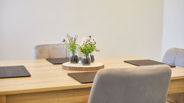 Una mesa de conferencias con jarrones de flores, soportes negros para tabletas y sillas grises.